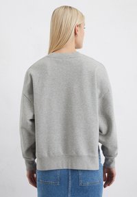 Felpa grigia chiara con una vestibilità comoda, spalle scese, polsini e orlo a coste. Lo sfondo è bianco puro.