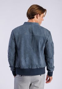 Chaqueta bomber de cuero azul para hombre con dobladillos y puños de náutica acanalados, que presenta un acabado texturizado y un parche en la parte superior de la espalda.