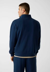 Pull-over en polaire bleu marine avec un col montant, des poignets et une base côtelés ; doté d'une bande contrastante marron clair en bas.