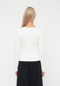 Witte lange mouwen top met een vierkante halslijn, aansluitend ontwerp en een gladde textuur. Gekleed met losse, donkere broeken met twee achterzakken.