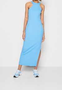 Blue sleeveless maxi dress in stretch fabric, featuring a side slit. Paired with light blue sneakers, showcasing a casual look.