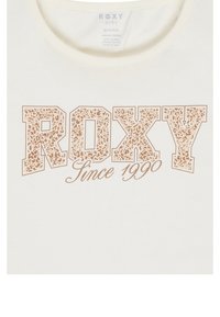Kermavalkoinen luomupuuvillapaita, jossa on rohkea leopardikuosisempi "ROXY" -logo vaaleassa beigeessä, ja alla kaunokirjoituksella kirjoitettu "Since 1990".