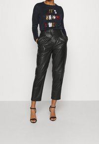 Pull marine avec texte en sequins et éléments décoratifs, associé à un pantalon en cuir noir taille haute et des talons noirs à lanières.