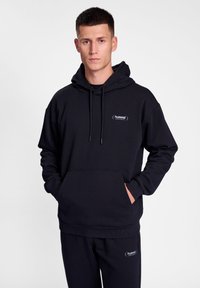 Svart hoodie i mjukt tyg, med en känguruficka, justerbar dragsko i huvan och en liten broderad logo på bröstet.