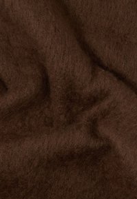 Tejido suave y esponjoso de color marrón oscuro con una textura peluda, que muestra pliegues y sombras en una superficie textil.