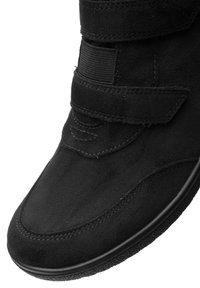 Zwarte suède schoen met een klittenbandsluiting en een ronde neus. Heeft contrasterende stiksels en een gemarmerde zwarte rubberen zool.