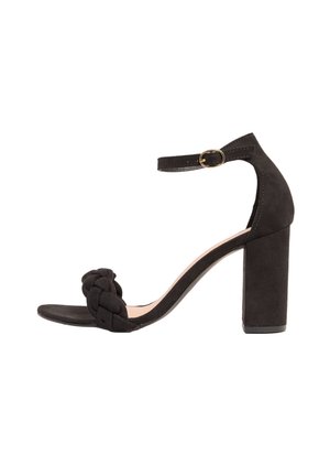 Sandal con tacco a blocco in suede nero, con cinturino anteriore intrecciato, punta aperta e cinturino alla caviglia con accentuazione in fibbia dorata.