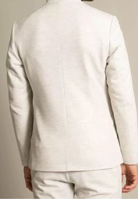 Ljusgrå blazer i strukturerad tyg, med hög krage och skräddarsydd passform, samt släta ärmar och sömdetaljer i ryggen.