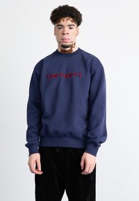 Sudadera azul marino con puños y dobladillo de canalé, con un destacado logo bordado en rojo "carhartt" en el pecho.
