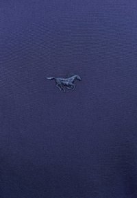 Marineblaues Gewebe mit glatter Textur zeigt eine gestickte Silhouette eines laufenden Pferdes in einem dunkleren Blauton.