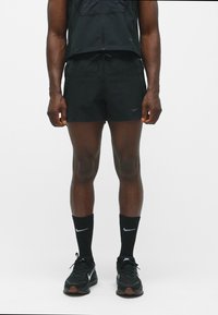 Schwarze Sportshorts und Socken mit Nike-Logo, getragen mit einer schwarzen zipfelbaren Weste. Die Shorts bestehen aus einem strukturierten Stoff und haben eine lässige Passform.