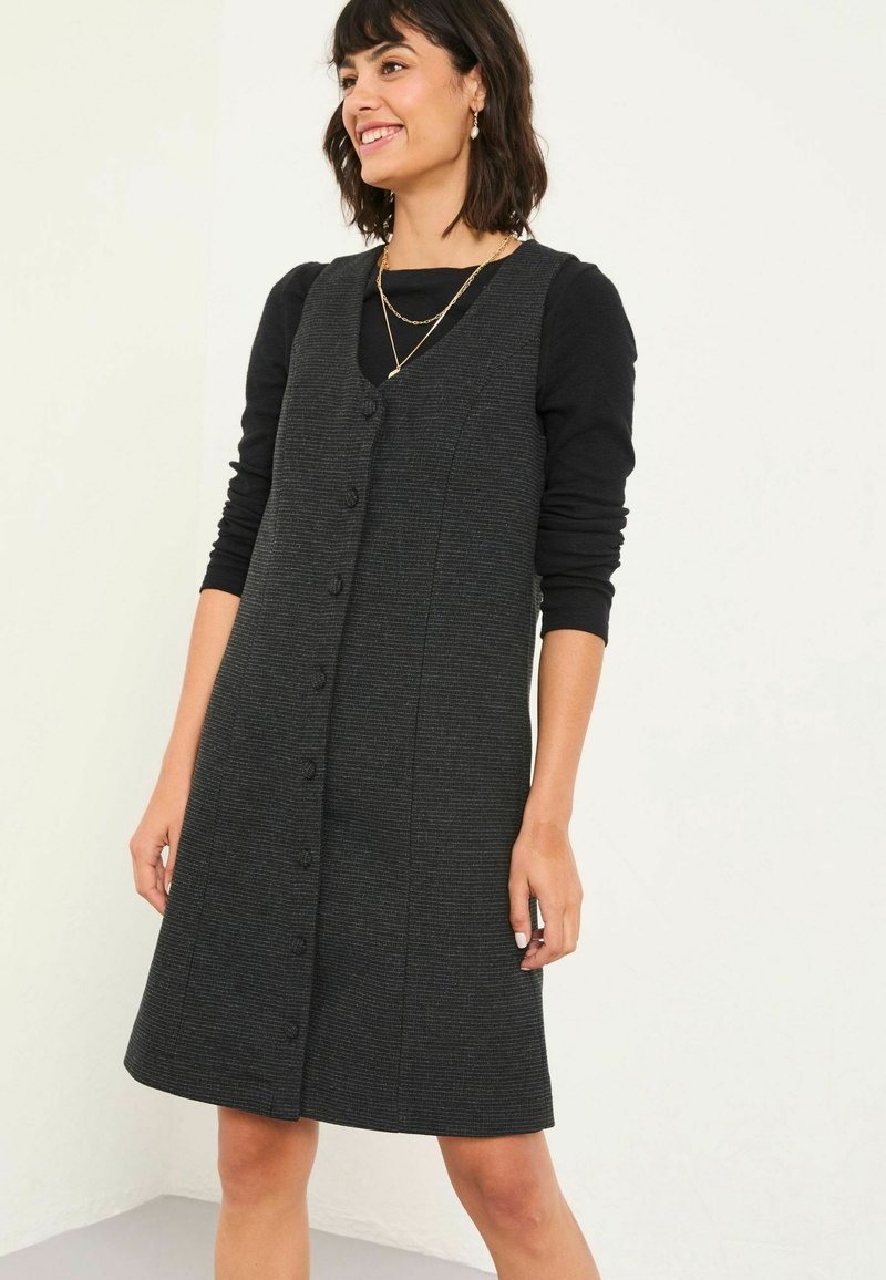 Graues ärmelloses Kleid aus strukturiertem Stoff, mit tailliertem Oberteil, durchgehender Knopfleiste und A-Linien-Rock. Getragen über einem schwarzen Langarmoberteil.