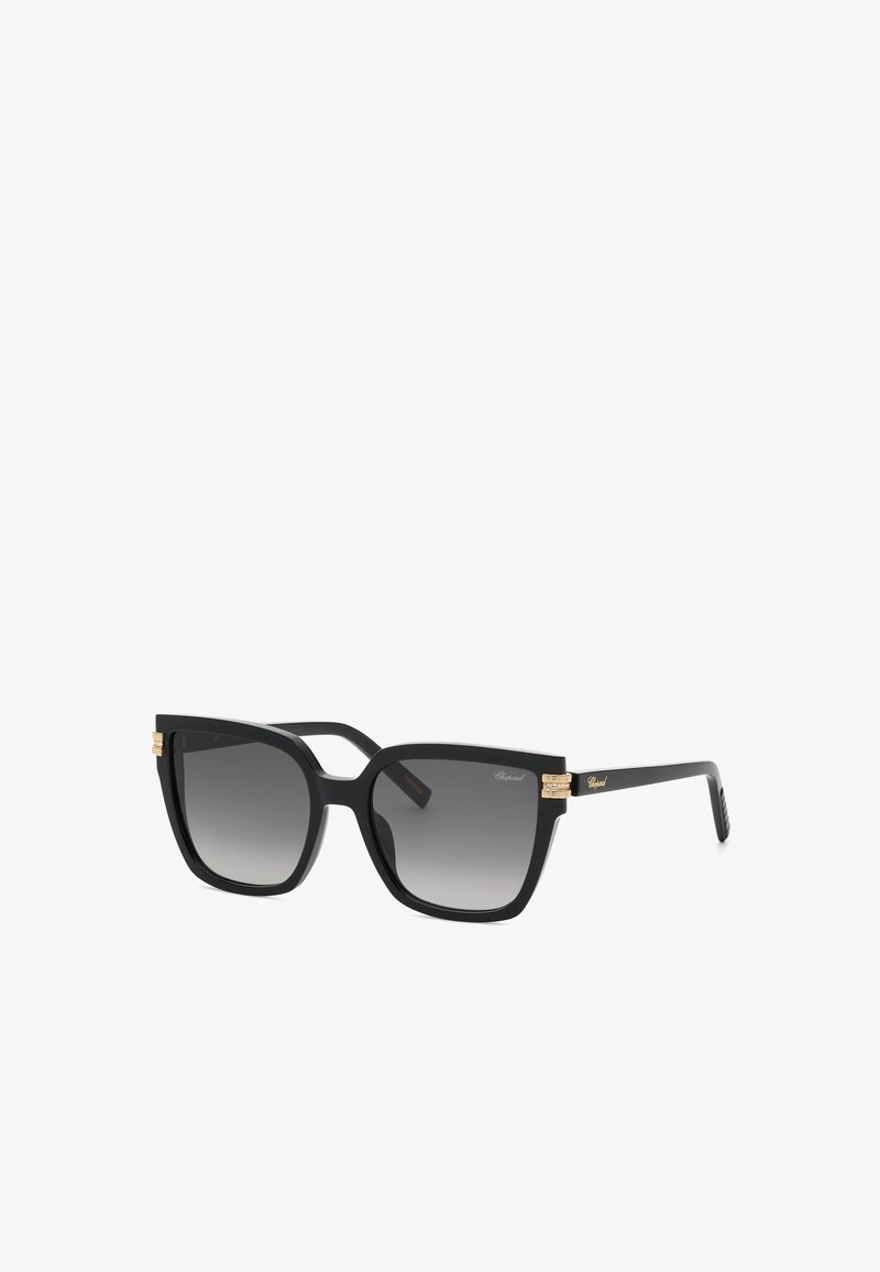 Lunettes de soleil carrées oversize noires avec verres foncés dégradés, charnières dorées et marquage subtil sur les branches.