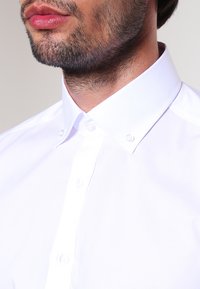 Weißes Hemd mit klassischem Kragen, glatter Textur und zwei Knöpfen, das dezente Nähdetails aufweist.