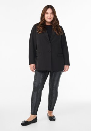 Blazer nero con vestibilità su misura, abbinato a leggings neri con stampa serpente. Indossato con ballerine nere con un piccolo dettaglio a fiocco.