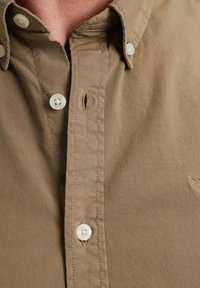 Bruine katoenen overhemd met knoopsluiting en een button-down kraag, met witte knopen en een klein geborduurd logo op de borst.