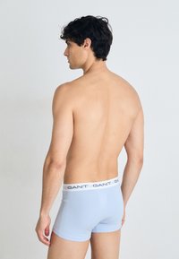 Helle blaue Boxershorts mit einem weißen elastischen Bund, der mit navyfarbenem Branding versehen ist. Glatte Textur, eng anliegendes Design, von hinten gezeigt.