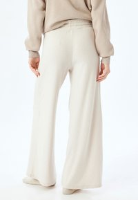 Pantalones de pernera ancha en tono beige claro, confeccionados en una suave tela texturizada con cinturilla. Presentan un ajuste holgado y un detalle mínimo para mayor comodidad.
