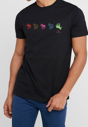 Zwart T-shirt met vijf kleurrijke geborduurde zebra's over de borst, waarvan de laatste ondersteboven, gedragen door een staande persoon.