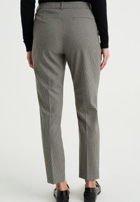 Skräddarsydda byxor i grå och svart houndstooth med rak benstil, med en bakficka och en slät yta. Bärs med svarta skor.