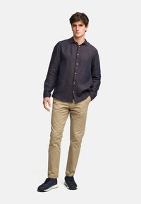 Camicia button-up azzurra in lino con maniche lunghe, abbinata a chinos beige e scarpe da ginnastica scure. Design semplice, vestibilità rilassata.