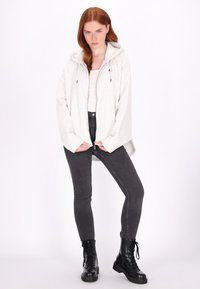 Lichtgrijze zip-up hoodie met verstelbare trekkoorden, gedragen over een witte top, gecombineerd met donkergrijze skinny jeans en zwarte veterschoenen.