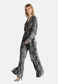 Un mono con estampado de flores en tela azul oscuro y dorada, con mangas largas, cintura ajustada con cinturón y pantalones de pierna ancha. Textura suave.