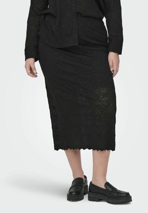 Sort, knælang nederdel med et tekstureret rosemønster. Har en bølget kant og er parret med sorte slip-on sko.