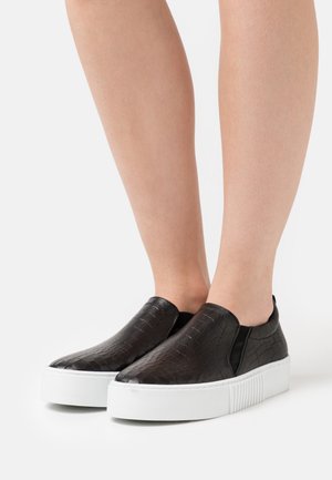 Sneakers neri slip-on con una finitura testurizzata a motivo coccodrillo, dotate di una suola platform bianca e accenti elastici sui lati.