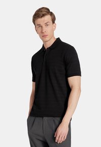 Czarna koszulka polo z teksturowanym wzorem, krótki rękaw i zapięcie na trzy guziki. Połączona z szarymi spodniami. Prosty i klasyczny design.