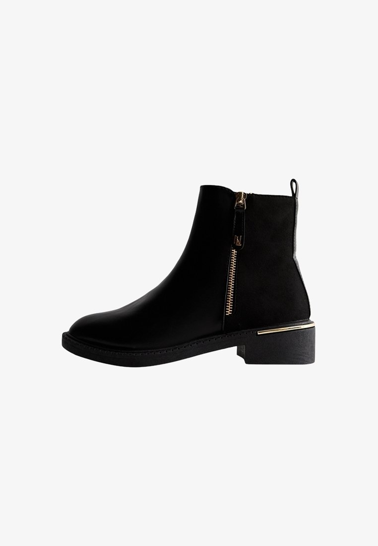 Bottine noire à fermeture éclair latérale, languette de tirage, talon carré bas, et détail métallique sur le bord du talon, présentée de profil sur fond blanc.