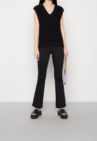 Svart ärmlös v-ringad topp med strukturerad stickning, i kombination med utsvängda svarta byxor, svarta kraftiga sandaler och en liten lavendelfärgad handväska.