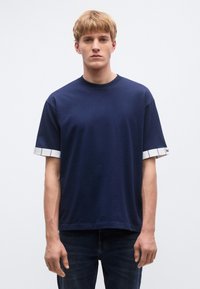 Tmavomodré bavlnené tričko s okrúhlym výstrihom a krátkymi rukávmi, s bielymi kockovanými vzormi na lemovaní rukávov.