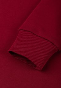 Bordeauxrode lange mouw manchetkraag met geribbelde textuur. Gladde, rekbare stof met een zachte afwerking en een nauwsluitende pasvorm bij de pols.