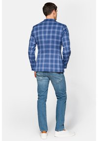 Niebieska marynarka w kratę o dopasowanym kroju, z klapami w kształcie notcha i pojedynczym rozcięciem, zestawiona z jasnymi dżinsami i białymi trampkami.