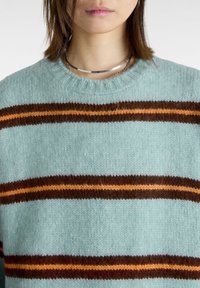 Maglione azzurro chiaro in morbido punto maglia con strisce orizzontali marroni e arancioni. Presenta un collo a girocollo a coste.