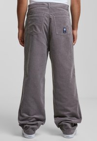 Grijze corduroy broek met brede benen, voor- en achterzakken, en een logo-label op de achterzak. Zachte textuur met verticale ribbel.
