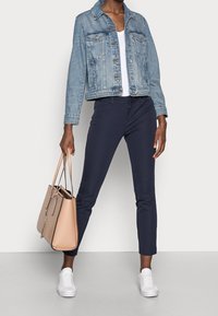 Jeansjacka, ljusblå, med två framfickor; vit t-shirt; navybyxor; beige tote bag; vita sneakers; slim-fit design.