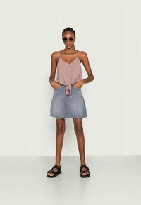 Pink sleeveless top with buttons and a knotted front, paired with a denim mini skirt. Worn with black sandals and sunglasses.