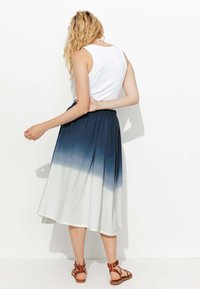 Jupe mi-longue avec un design dégradé, passant d'un bleu marine foncé en haut à un blanc en bas ; taille élastique, texture douce.