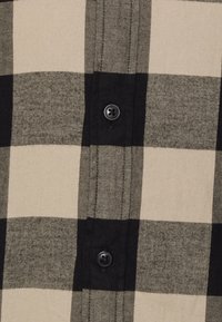 Camisa de cuadros en blanco y negro con grandes patrones de cuadros y un botón negro en el frente. Textura de tela suave.