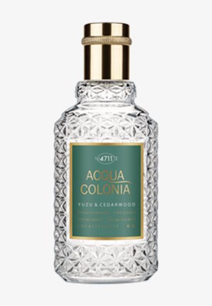 Botella de perfume de vidrio transparente con tapa dorada y etiqueta verde que dice "Acqua Colonia Yuzu & Cedarwood".