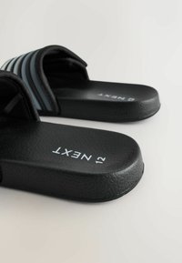 Sandale negre de tip papuc cu tălpi texturate, având partea superioară cu dungi negre și albastre și un design plat. Numele mărcii „NEXT” este imprimat pe tălpi.