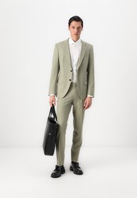 Traje verde claro con una chaqueta estructurada y pantalones a juego, combinado con una camisa blanca y zapatos de cuero negros, sosteniendo un bolso tote negro.