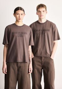 Brune bomuld T-shirts med broderet "TOMMY JEANS" logo, afslappet pasform, korte ærmer, kombineret med matchende brune bukser.