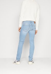 Ljust blå denimjeans med slim fit, har två bakfickor och en läderlapp på midjan. Matchas med en vit långärmad topp.