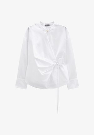 Biała koszula z długim rękawem z gładkiego materiału, z okrągłym dekoltem i asymetrycznymi marszczeniami zapinanymi na tasiemkę w talii.