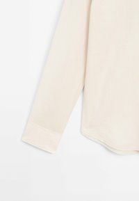 Lyse beige langærmet skjorte med et blødt, struktureret stof. Har en buet kant og manchet detaljer. Glat finish hele vejen igennem.