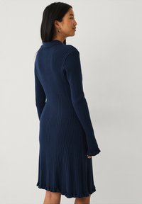 Navy-blaues, geripptes Strickkleid mit langen Ärmeln, einem kragenlosen Ausschnitt und einem schwingenden Saum. Verfügt über einen strukturierten Stoff und eine figurbetonte Silhouette.