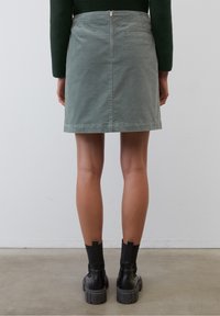 Jupe mini en coton gris avec une fermeture éclair à l'arrière, présentant un design épuré et une forme légèrement structurée, associée à des bottines noires.